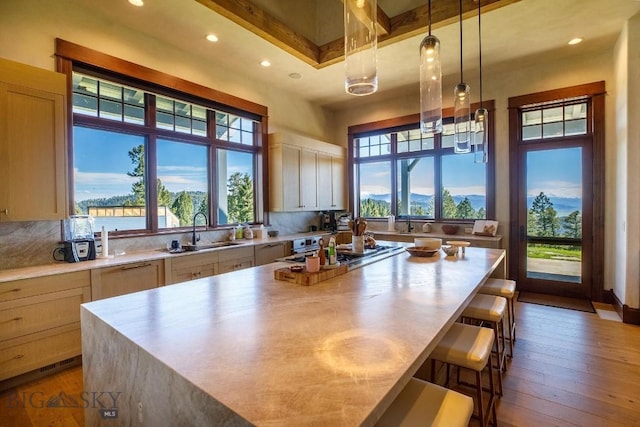 kitchen with sink, light brown cabinets, a kitchen breakfast bar, a kitchen island, and hardwood / wood-style flooring