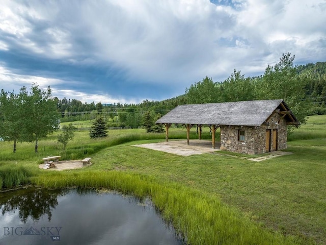 view of home's community with a water view, a lawn, and an outbuilding