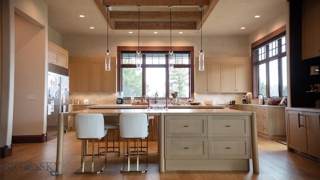 kitchen with a raised ceiling, a kitchen island with sink, light hardwood / wood-style floors, and stainless steel built in fridge