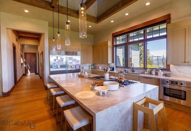 kitchen with a kitchen island, appliances with stainless steel finishes, hanging light fixtures, light brown cabinets, and light hardwood / wood-style flooring