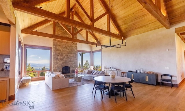 dining area featuring a stone fireplace, high vaulted ceiling, light hardwood / wood-style floors, wooden ceiling, and beam ceiling