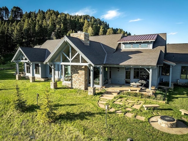 rear view of house featuring a patio, a lawn, and a fire pit