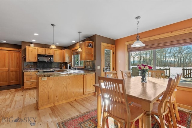 kitchen featuring pendant lighting, dark stone counters, sink, backsplash, and light wood-type flooring