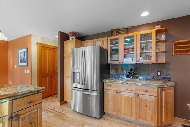 kitchen with stainless steel refrigerator with ice dispenser, tasteful backsplash, light wood-type flooring, and light stone countertops