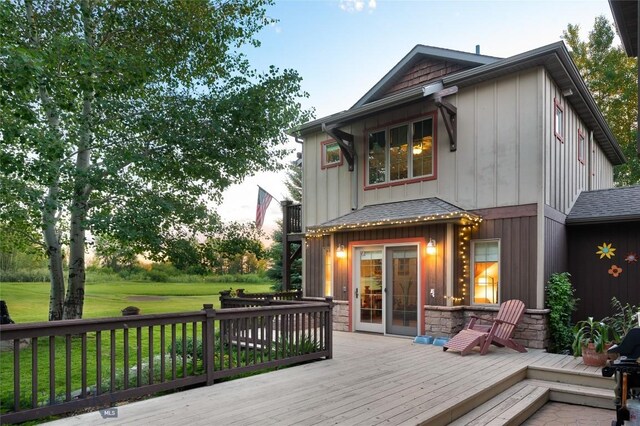 back house at dusk featuring a wooden deck and a yard