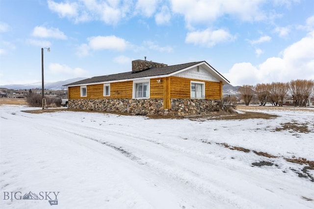 snow covered property featuring stone siding and a chimney