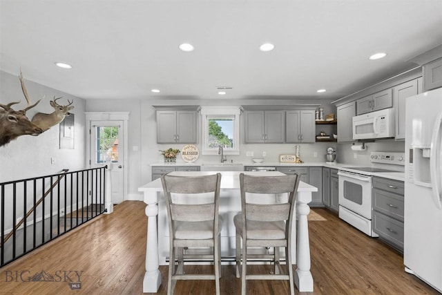 kitchen featuring dark wood-type flooring, white appliances, a breakfast bar area, and gray cabinetry