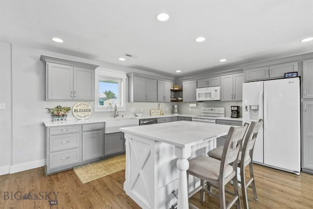 kitchen featuring sink, a kitchen bar, a center island, light hardwood / wood-style floors, and white appliances