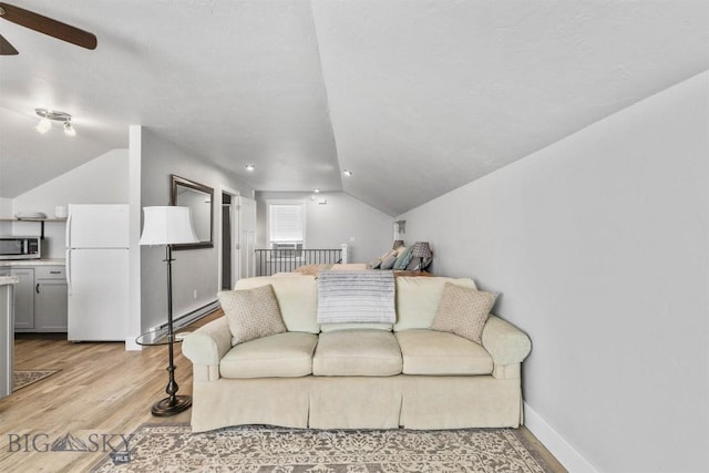 living room featuring vaulted ceiling, ceiling fan, light hardwood / wood-style floors, and a baseboard heating unit