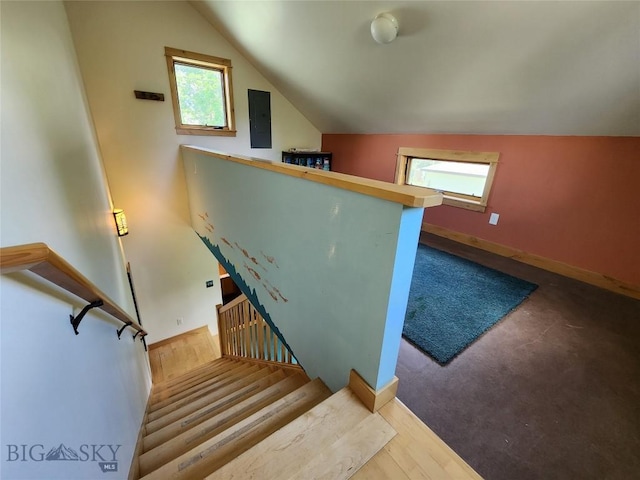 stairs with electric panel, wood-type flooring, vaulted ceiling, and a healthy amount of sunlight