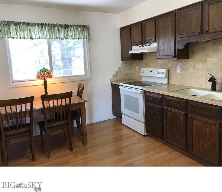 kitchen featuring white electric stove, decorative backsplash, dark brown cabinetry, a sink, and under cabinet range hood