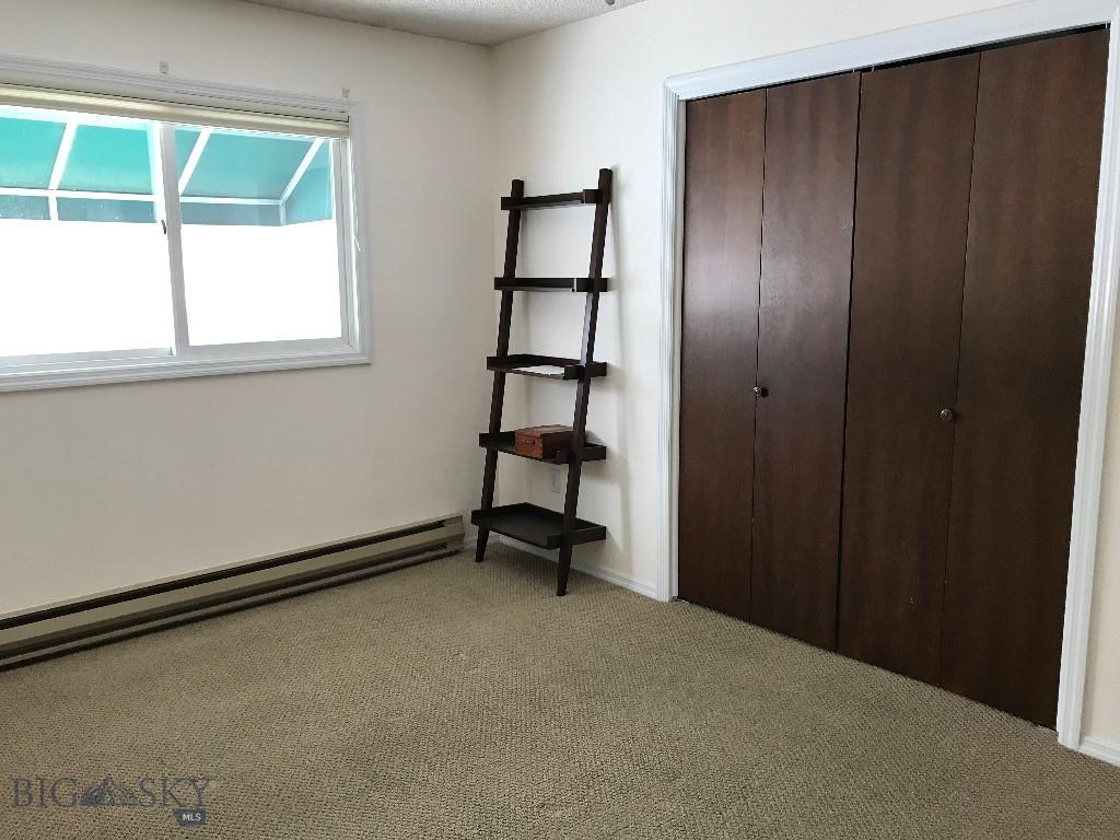 unfurnished bedroom with a baseboard heating unit, a closet, and light colored carpet