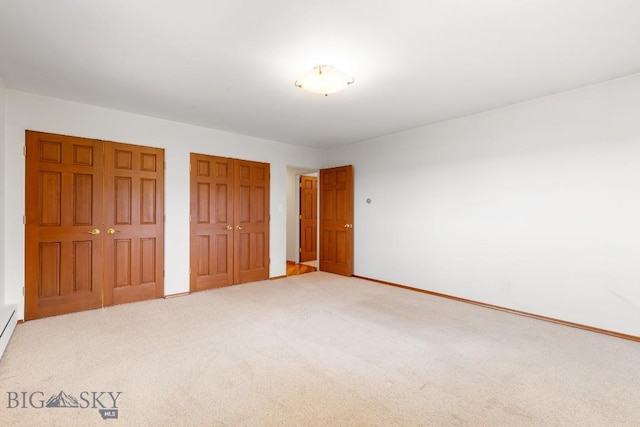 unfurnished bedroom featuring multiple closets, carpet floors, and a baseboard radiator