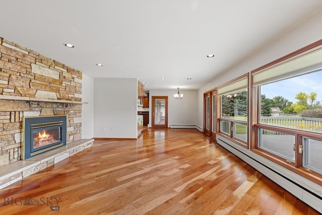 unfurnished living room featuring light wood-type flooring, baseboard heating, a stone fireplace, and a notable chandelier