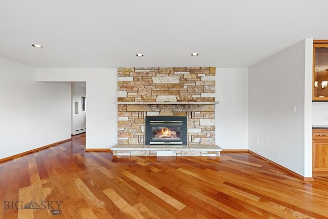 unfurnished living room featuring a baseboard heating unit, a fireplace, and wood-type flooring