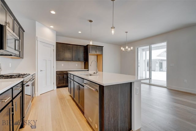 kitchen with appliances with stainless steel finishes, an inviting chandelier, an island with sink, sink, and dark brown cabinets