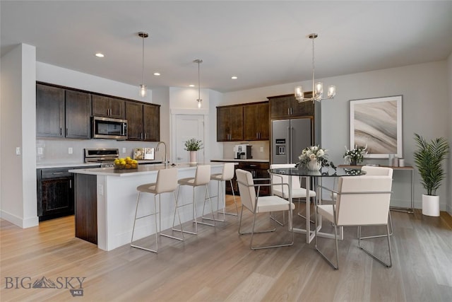 kitchen with pendant lighting, light wood-type flooring, stainless steel appliances, and an island with sink