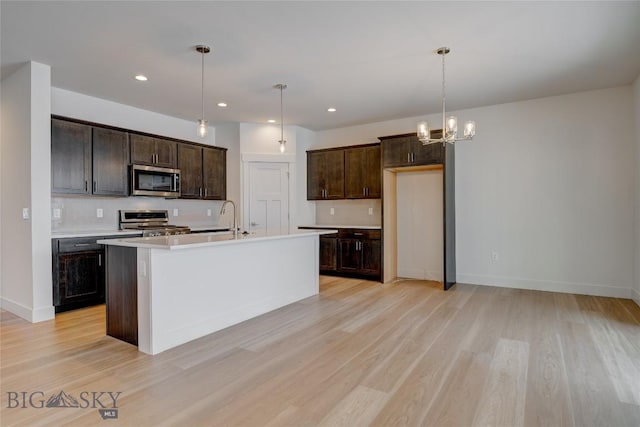 kitchen featuring backsplash, a center island with sink, hanging light fixtures, light wood-type flooring, and appliances with stainless steel finishes