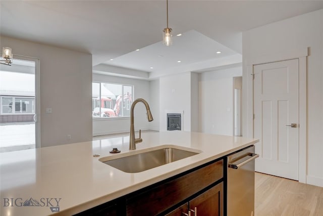 kitchen featuring hanging light fixtures, light wood-type flooring, dishwasher, and sink