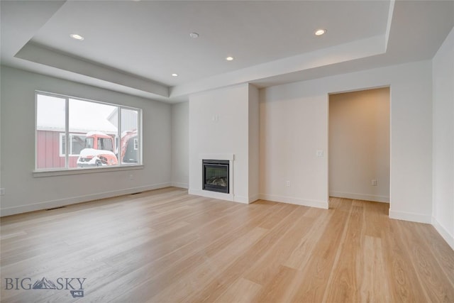 unfurnished living room featuring a raised ceiling and light hardwood / wood-style floors