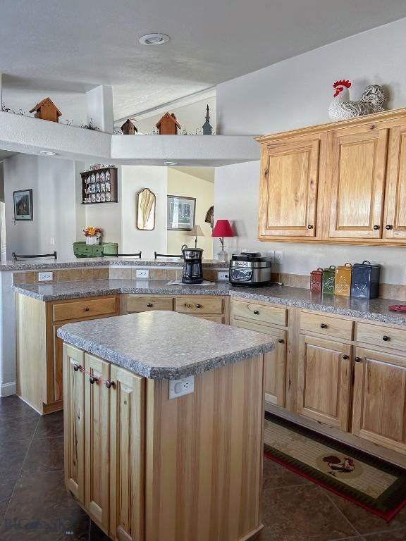 kitchen featuring light brown cabinetry, vaulted ceiling, kitchen peninsula, a kitchen island, and dark tile patterned floors