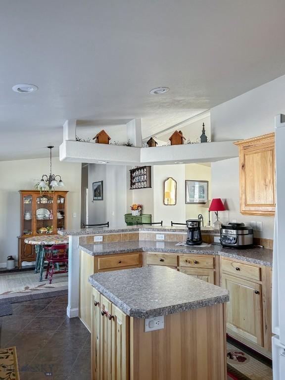 kitchen with lofted ceiling, light brown cabinetry, decorative light fixtures, dark tile patterned flooring, and a kitchen island