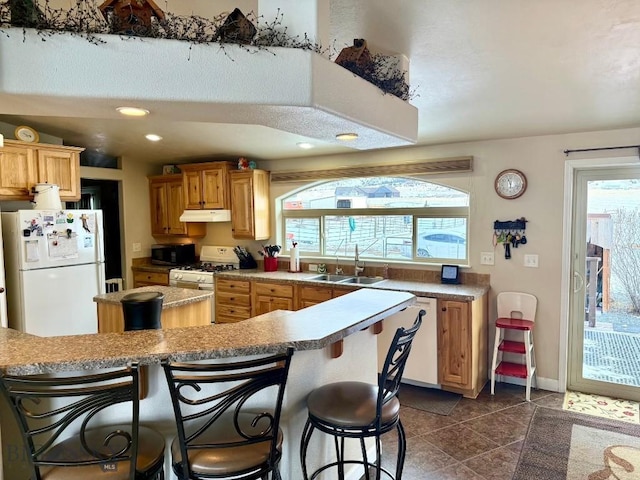 kitchen featuring sink, a breakfast bar area, dark tile patterned flooring, white appliances, and a healthy amount of sunlight