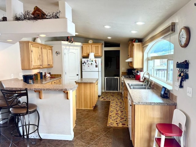 kitchen featuring a breakfast bar, light brown cabinetry, sink, white refrigerator, and kitchen peninsula