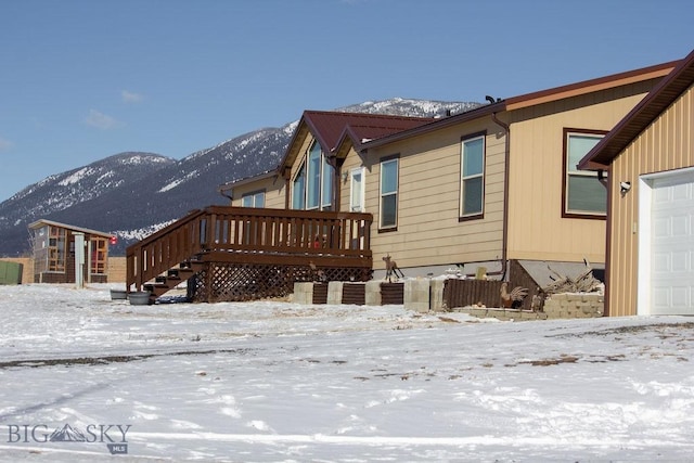 snow covered rear of property with a garage and a deck with mountain view