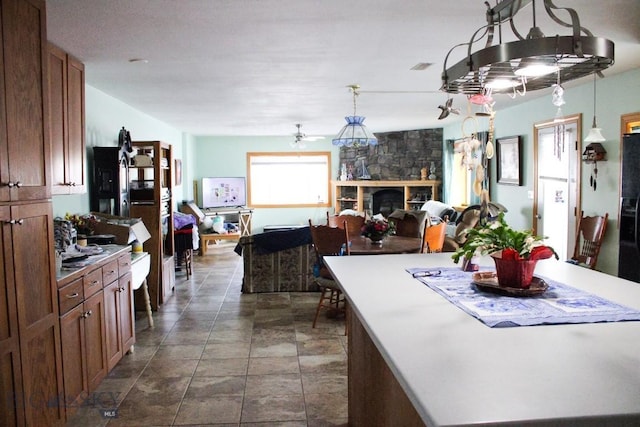 kitchen with a fireplace, a kitchen island, a ceiling fan, open floor plan, and brown cabinetry