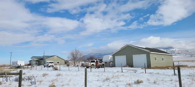 yard layered in snow with a detached garage, fence, a mountain view, and an outdoor structure