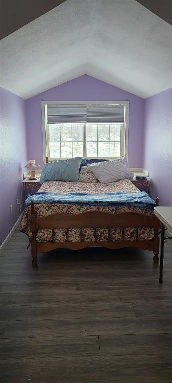 bedroom featuring vaulted ceiling, dark wood-type flooring, a textured ceiling, and baseboards