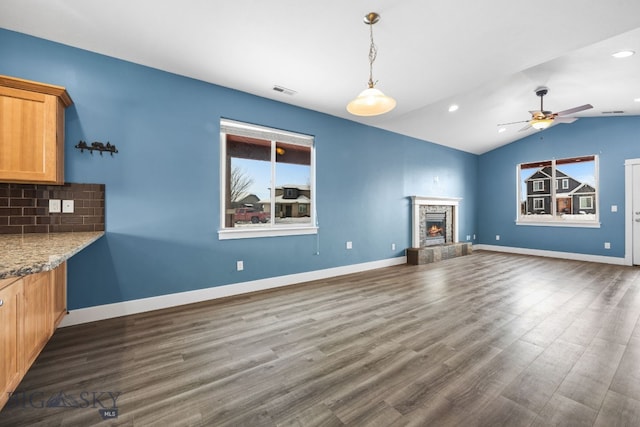 unfurnished living room featuring a warm lit fireplace, dark wood-style flooring, lofted ceiling, and baseboards