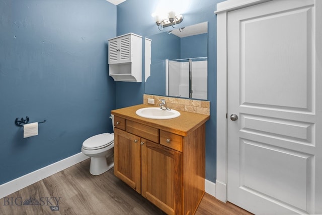 bathroom with toilet, wood finished floors, vanity, baseboards, and walk in shower