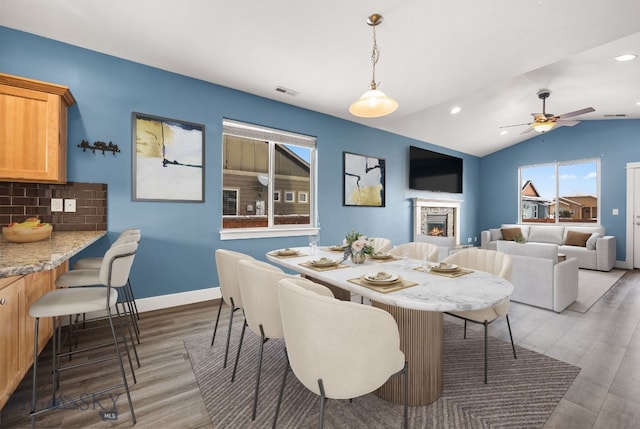 dining area featuring vaulted ceiling, ceiling fan, dark hardwood / wood-style flooring, and a stone fireplace