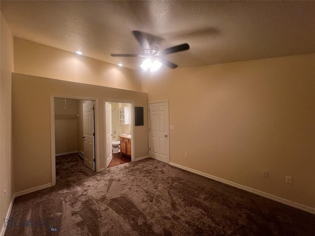 unfurnished bedroom featuring ceiling fan, dark colored carpet, ensuite bath, a closet, and a walk in closet