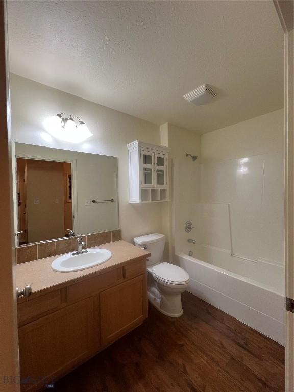 full bathroom featuring toilet, hardwood / wood-style floors,  shower combination, a textured ceiling, and vanity