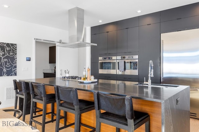 kitchen with a large island with sink, appliances with stainless steel finishes, sink, a kitchen breakfast bar, and island range hood