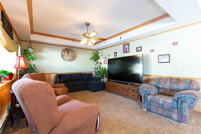 carpeted living room featuring a raised ceiling, ceiling fan, crown molding, and wainscoting