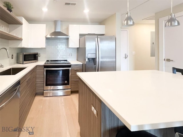 kitchen with stainless steel appliances, pendant lighting, white cabinetry, and wall chimney exhaust hood