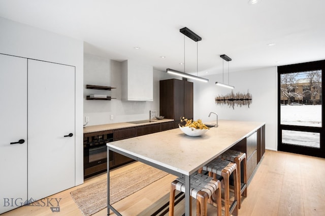 kitchen with a kitchen island with sink, light wood-type flooring, pendant lighting, white cabinets, and black appliances