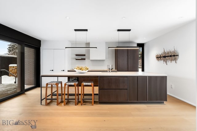 kitchen with white cabinets, decorative light fixtures, plenty of natural light, light wood-type flooring, and a center island with sink