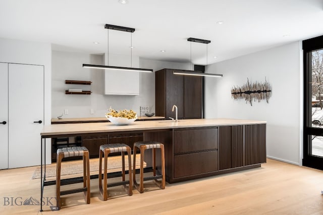 kitchen featuring dark brown cabinetry, white cabinetry, light hardwood / wood-style floors, hanging light fixtures, and a kitchen island with sink