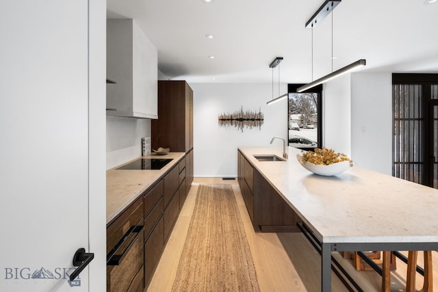 kitchen with light hardwood / wood-style floors, black appliances, pendant lighting, sink, and a kitchen breakfast bar