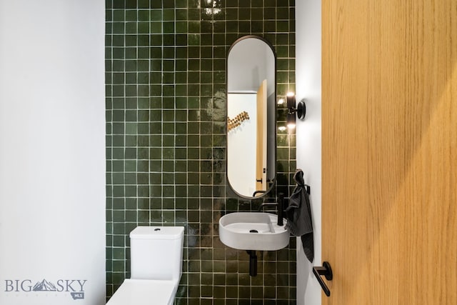 bathroom featuring toilet, tile walls, and sink