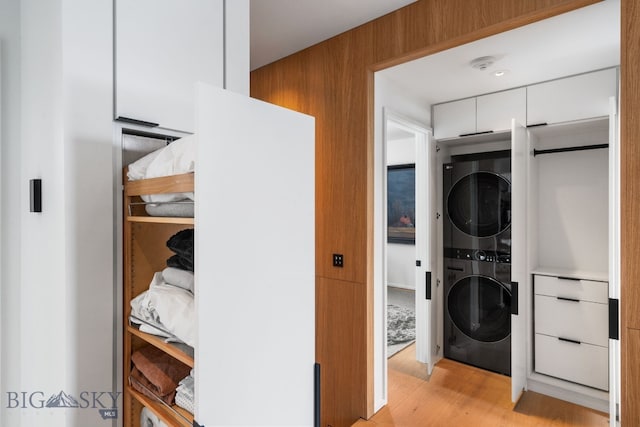 laundry room with stacked washing maching and dryer and light hardwood / wood-style floors