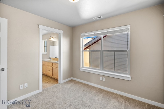 unfurnished bedroom featuring ensuite bathroom, light colored carpet, sink, and multiple windows