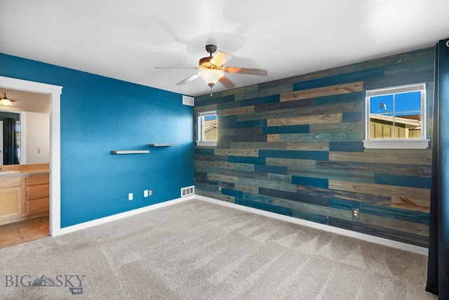 carpeted spare room featuring ceiling fan, wood walls, and sink