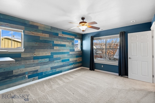 carpeted empty room with ceiling fan, a healthy amount of sunlight, and wood walls