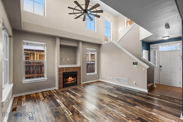 unfurnished living room featuring ceiling fan, a high ceiling, dark hardwood / wood-style floors, and a fireplace